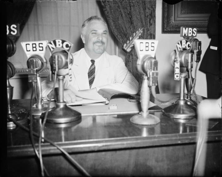 black and white photo of president goldberg surrounded by mics